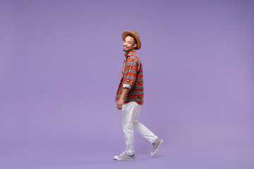 Fototapeta na wymiar Side view of smiling young african american guy in casual colorful shirt hat posing isolated on violet background studio. People sincere emotions lifestyle concept. Mock up copy space. Looking camera.