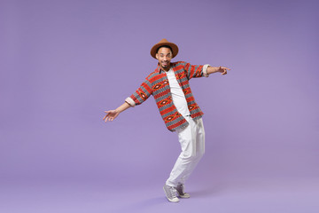 Smiling young african american guy in casual colorful shirt hat posing isolated on violet...