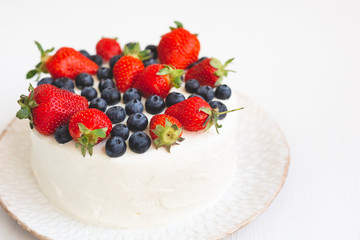 Close-up of white cream cake decorated with strawberries and blueberries on white handmade plate