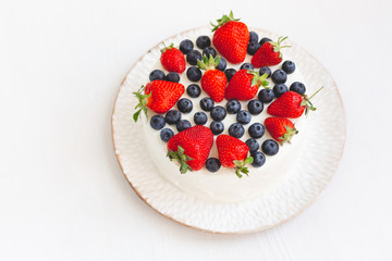 A beuutiful tasty home made cake or pie on beautiful white plate on light wooden background. Dessert is decorated with summer berries, strawberries and blueberries