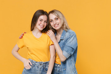 Two smiling young women girls friends in casual t-shirts denim clothes posing isolated on yellow background studio portrait. People sincere emotions lifestyle concept. Mock up copy space. Hugging.
