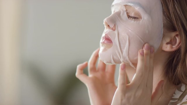  Slowmo close up of beautiful young woman rubbing sheet face mask after applying it in morning
