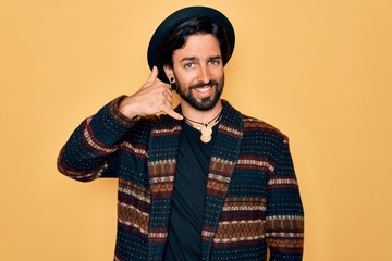 Young handsome hispanic bohemian man wearing hippie style and boho hat smiling doing phone gesture...