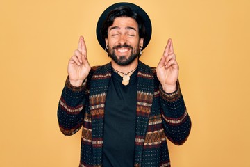 Young handsome hispanic bohemian man wearing hippie style and boho hat gesturing finger crossed...