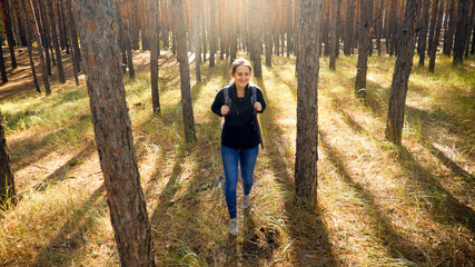 Beautiful smiling girl walking between pine trees while hiking in forest on sunny day