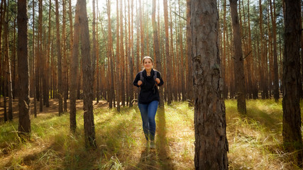 Beautiful smiling woman enjoying hiking in pine forest on sunny autumn day