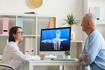 Side view portrait of female doctor consulting senior patient while sitting at desk in modern clinic interior, copy space