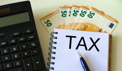 TAX word in a notebook against the background of calculitar and banknotes