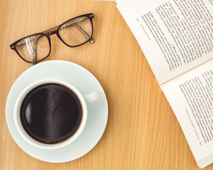 Flat lay, Office table wooden desk, Bright Creative workspace with eyeglasses, book and a cup of black coffee, Top view with copy space