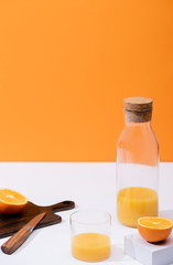 fresh orange juice in glass and bottle near cut fruit on wooden cutting board with knife on white surface isolated on orange