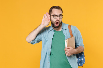 Shocked young man student in casual clothes glasses with backpack hold books isolated on yellow...