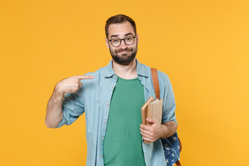 Smirked young man student in casual clothes glasses backpack hold books isolated on yellow background in studio. Education in high school university college concept. Pointing index finger on himself.