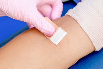 Nurse hand is glueing an adhesive plaster on arm after blood sampling,