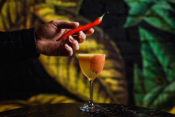 Putting red hot chili pepper garnish on a cocktail glass with a drink