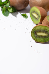 Fototapeta na wymiar selective focus of fresh kiwi fruits near green peppermint and black seeds on white