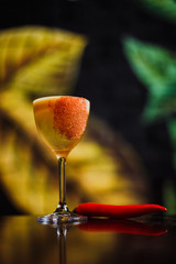 A cocktail in a nick and nora glass garnished with red hot chili pepper