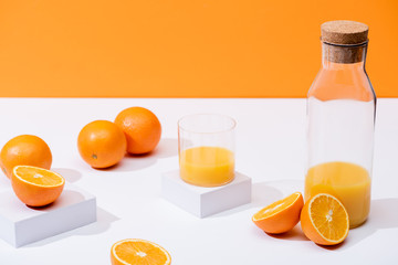 fresh orange juice in glass and bottle near ripe oranges on white surface isolated on orange