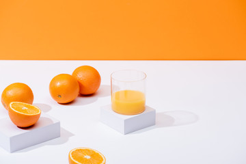 fresh orange juice in glass near ripe oranges on white surface isolated on orange