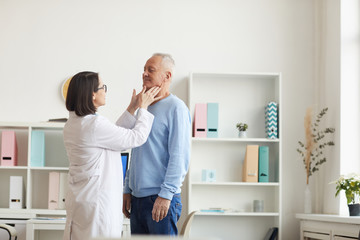 Wide angle portrait of female doctor palpating neck of senior patient while examining him during...