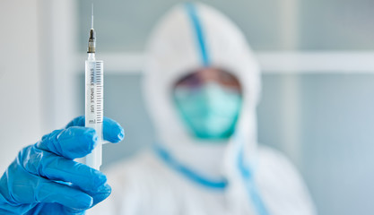Forscher in Schutzkleidung im Labor hält Spritze zur Impfung