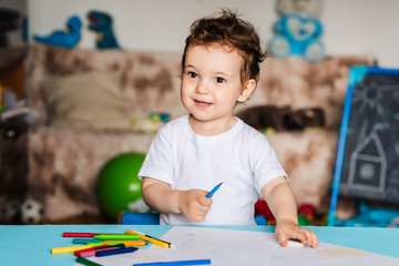 a small boy draws on sheets of paper lying on the table with colored pencils