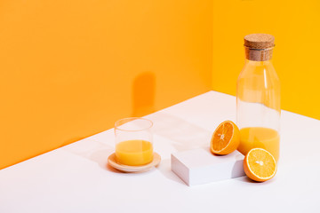 fresh orange juice in glass and bottle near ripe oranges on white surface on orange background