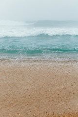 Aqua blue ocean waves background. Сlear water on sandy beach. Foggy weather. Copy space for text. Vertical photo.