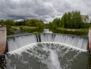 Waterfall on an old dam in the forest under a cloudy sky