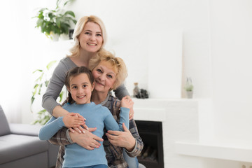 Portrait of three generations of women look at camera posing for family picture, cute little girl hug mom and granny enjoy time at home, smiling mother, daughter and grandmother spend weekend together