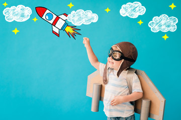Happy child playing with toy paper wings against blue background