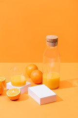 fresh orange juice in glass and bottle near ripe oranges and white cubes isolated on orange