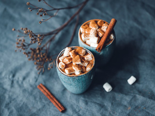 Hot chocolate with marshmallow and cinnamon in blue ceramic cups on a table. The concept of cosy holidays and New Year.