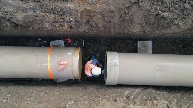 Concrete pipe tube installation. Aerial above men at work outside with heavy machinery to connect and install water or sewerage pipeline in a digging soil land