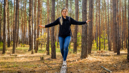Beautiful young woman with backpack crossing the ravine in forest by balancing on tree log