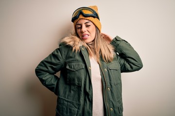 Young brunette skier woman wearing snow clothes and ski goggles over white background Suffering of neck ache injury, touching neck with hand, muscular pain