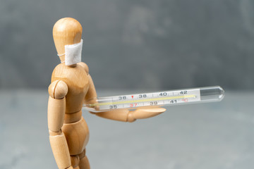 Wooden mannequin in a medical mask with a thermometer in his hands.