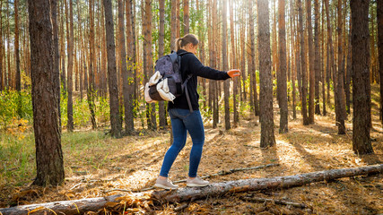 Young female hiker walking and balancing on fallen tree log in forest