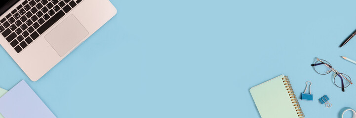 Top view of laptop and stationery on a blue pastel background. Workspace concept banner with place for text.