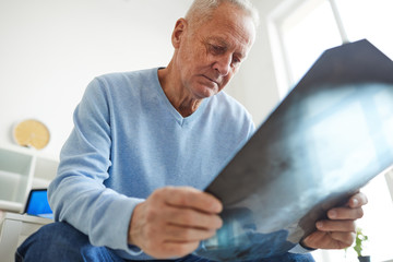 Low angle view at senior man holding x-ray image while waiting for consultation in clinic