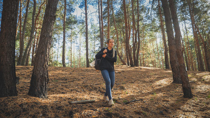 Toned photo of tired female tourist with heavy backpack walking on hiking route in forest