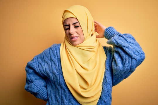 Young beautiful brunette muslim woman wearing arab hijab over isolated yellow background Suffering of neck ache injury, touching neck with hand, muscular pain