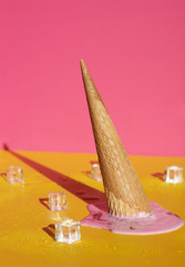 Strawberry ice cream cone upside down and melted. Behind it is a yellow and blue background.