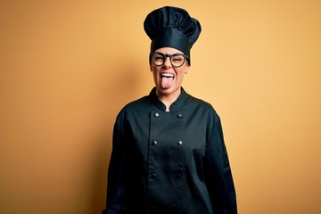 Young beautiful brunette chef woman wearing cooker uniform and hat over yellow background sticking...