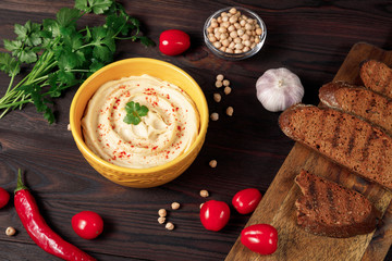 Plate of traditional hummus with crispy bread on wooden background