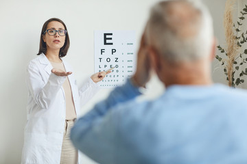 Waist up portrait of young female ophthalmologist pointing at eye chart while testing eyesight of...