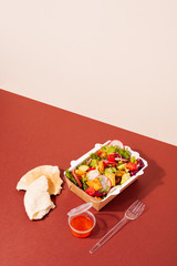 Healthy fresh vegetarian Fattoush salad in take away packaging box on red and beige background. Delivery restaurant authentic food concept