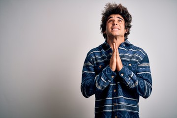 Young handsome man wearing casual shirt standing over isolated white background begging and praying...