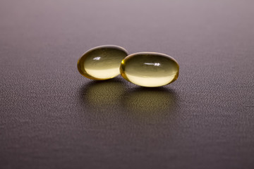 two yellow transparent omega-3 capsules lie against a dark background