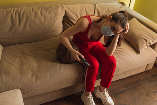 Upset Sportswoman In Medical Mask Holding Remote Controller Near Basketball While Watching Championship In Living Room