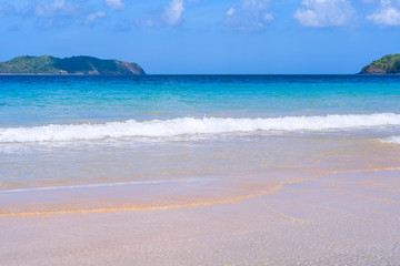 Obraz premium Beautiful amazing gold colored sandy beach with soft waves isolated with sunny blue sky. Concept of tropical calm tourism idea, copy space, close up